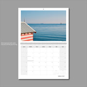 A3 Wall Calendar: Captivating Vistas featuring calm blue-green waters with a lone bathing box, candy striped pink in the foreground 