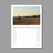 A3 Wall Calendar: Captivating Vistas featuring a couple with dog walking along the beach at golden hour with the city skyline as a backdrop