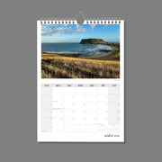 A4 Wall Calendar: Golden Hour featuring spectacular coastline with large volcanic rock as highlight and golden grass in foreground