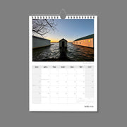 A4 Wall Calendar: Golden Hour featuring 3 boathouse buildings over water at sunset with one bathed in golden light 