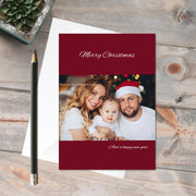 Customised Card: Festive - a card featuring a happy couple and baby in a Christmas setting, red colour background and Christmas greeting