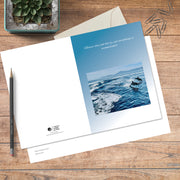 A6 greeting card in colour with full spread displayed on timber, featuring dolphins swimming and a nature quote