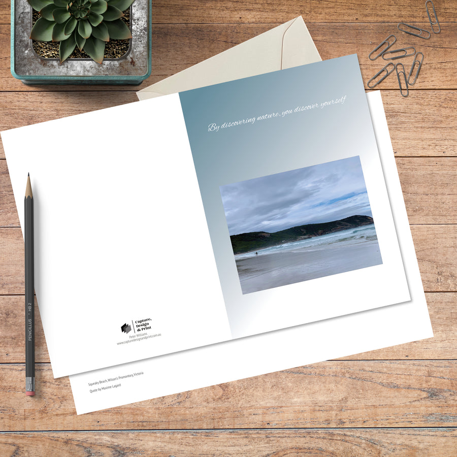 A6 greeting card in colour with full spread displayed on timber, featuring a lone surfer on the beach and a nature quote