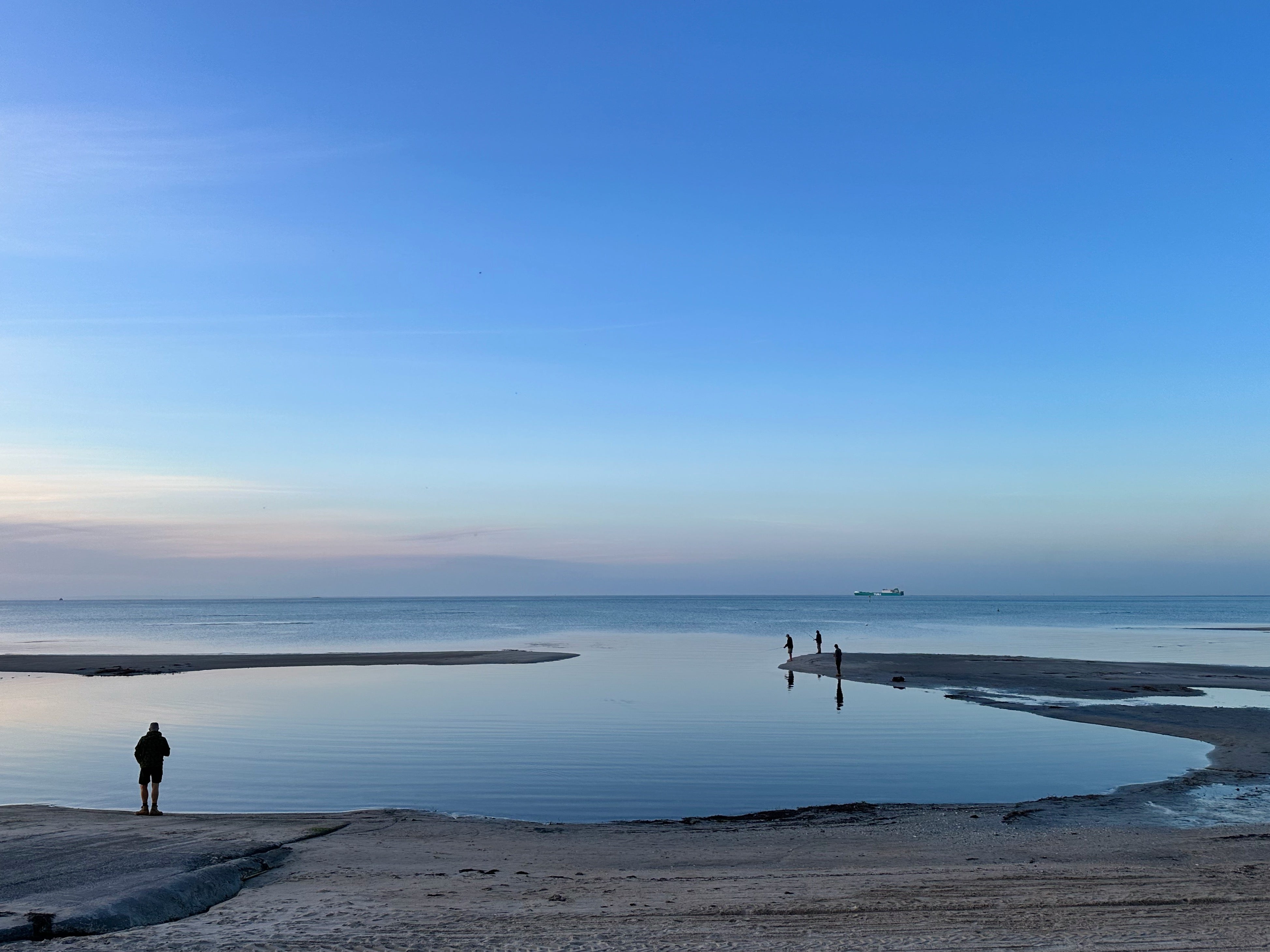 fishermen are silhouetted on the sandbank at low tide in twilight