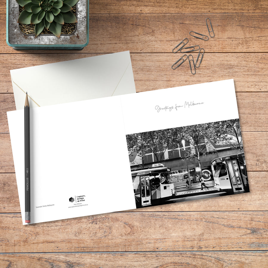 A small square greeting card in B&W with full spread displayed on timber, featuring two Melbourne trams head to head