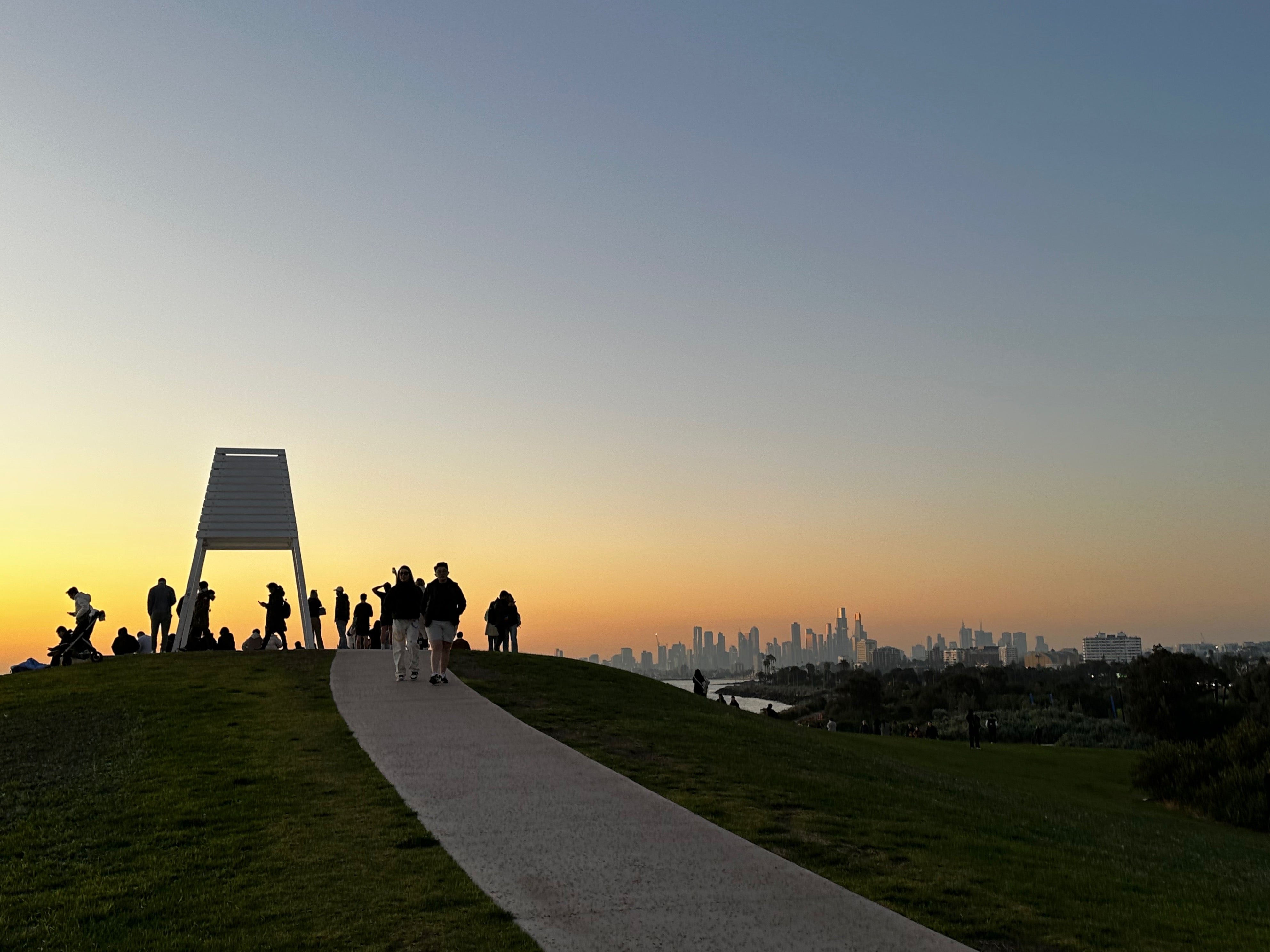 View of path leading uphill to a small landmark where people are gathering to take photos at sunset