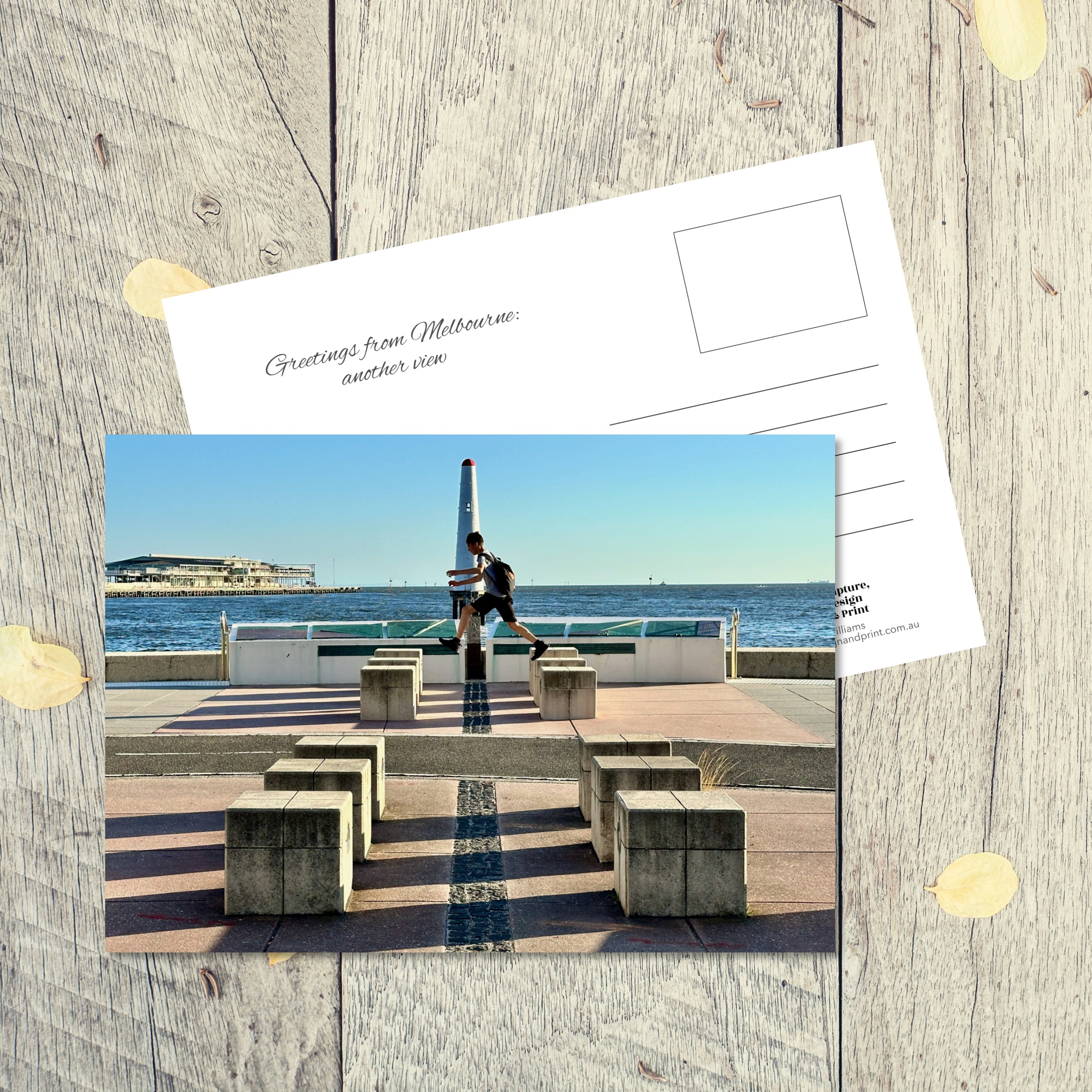 Postcard from Melbourne: Another View, featuring a boy leaping over cement blocks on the promenade adjacent to the bay at Port Melbourne