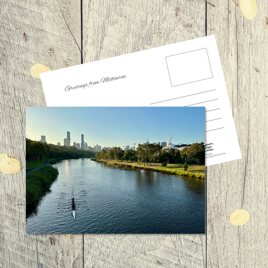 Postcard from Melbourne: Yarra River, a landscape postcard featuring a lone kayak on the cool blue river next to parklands in early evening