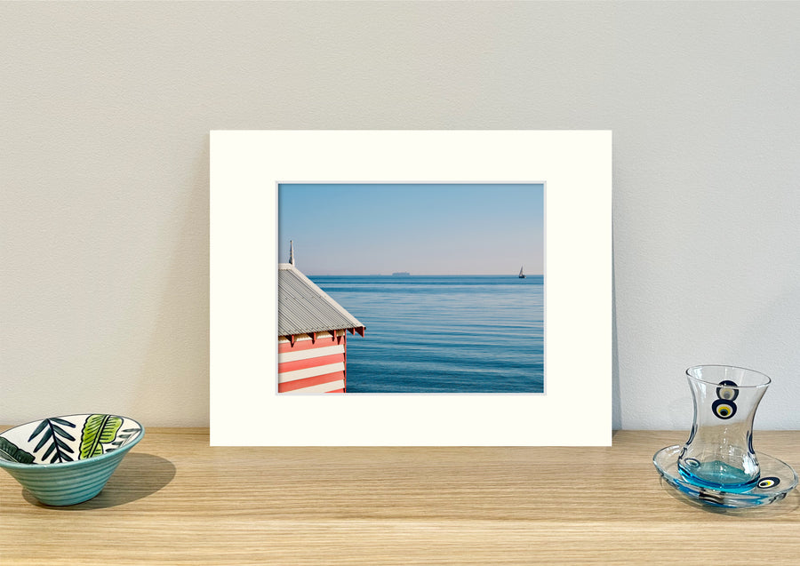 Frame mount containing a colour print of a red and white bathing box against a vivid blue backdrop standing  upright on sideboard