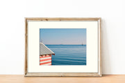 Frame mount with print of red and white bathing box against vivid blue waters in finalised picture frame on sideboard