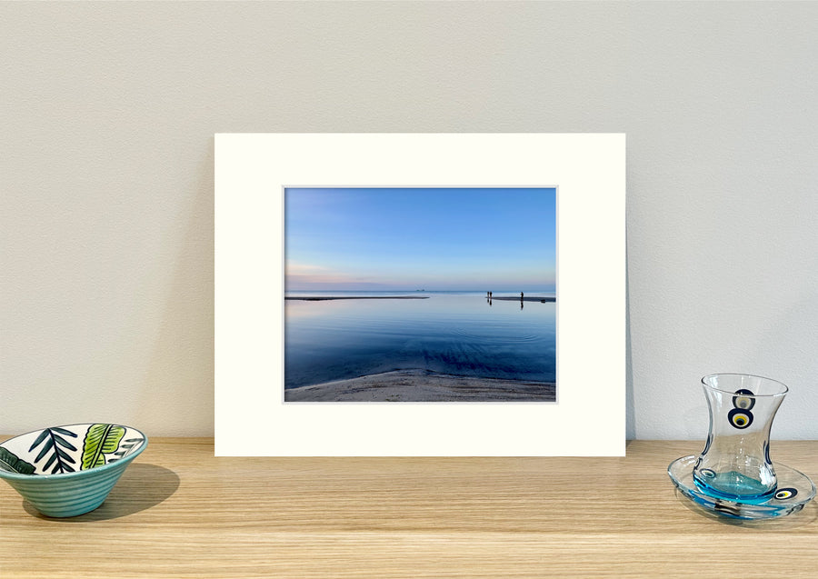 Frame mount containing a colour print of fisherman in shallow waters and a pretty sky upright on sideboard