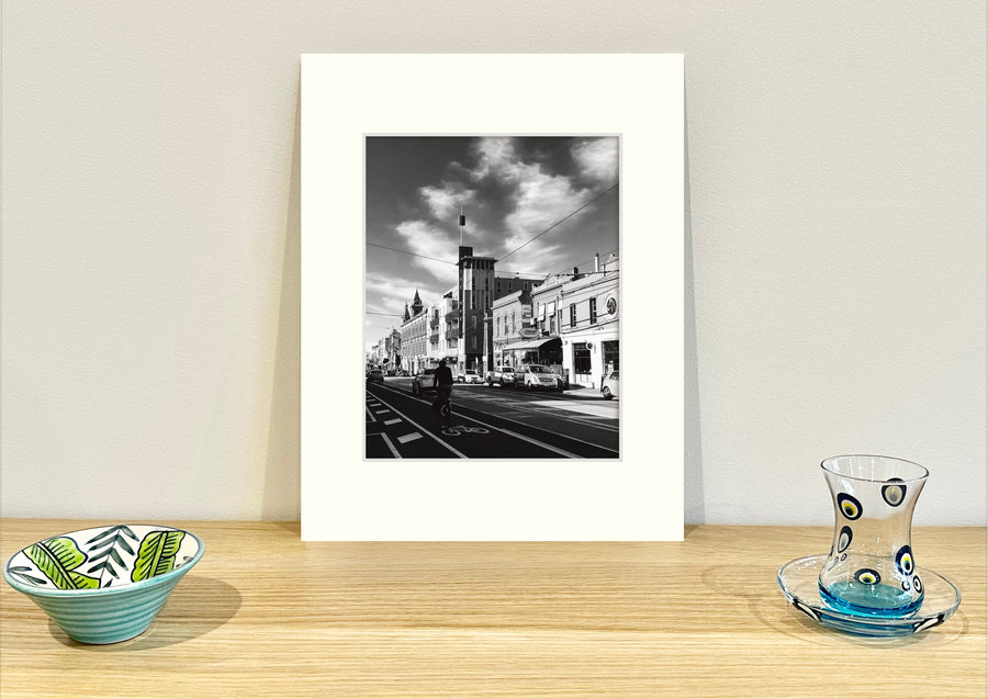 Frame mount containing a B&W print of Brunswick St, Fitzroy sitting upright on sideboard with objets d’art to the sides