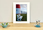 Frame mount containing a colour print of a part of a lighthouse against a backdrop of water standing  upright on sideboard