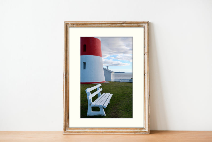 Frame mount with print of a part of a lighthouse against a backdrop of water in finalised picture frame on sideboard