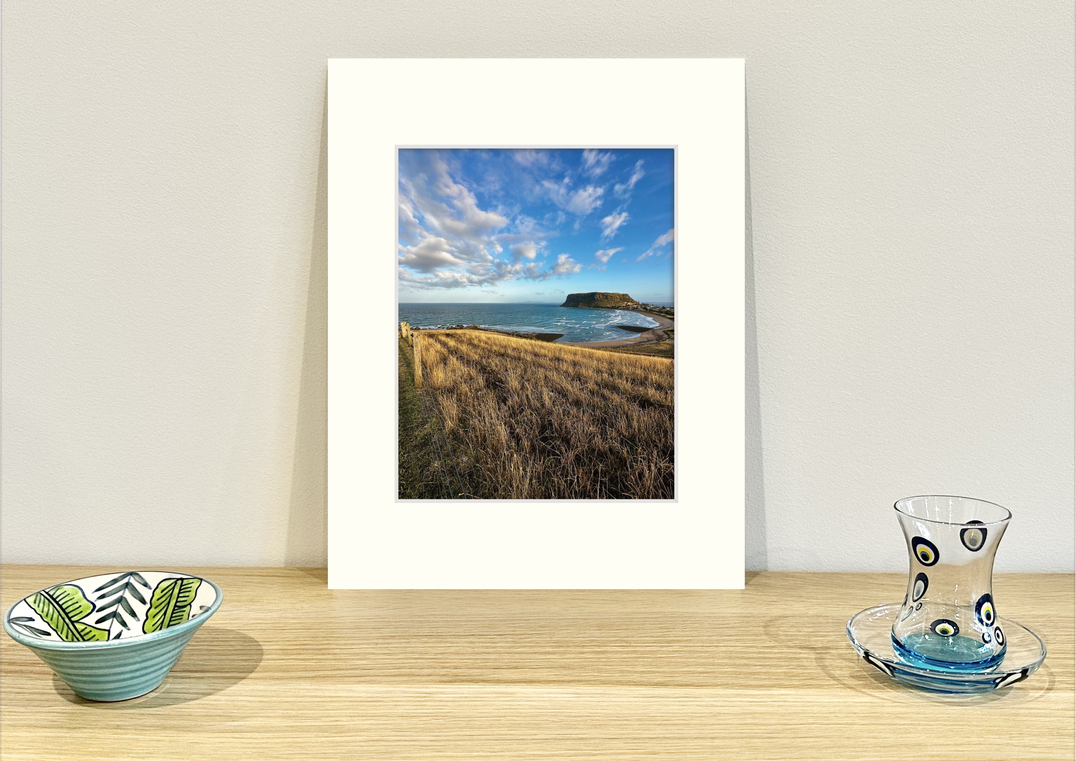 Frame mount containing a colour print of scenic Stanley, Tasmania sitting upright on sideboard with objets d’art to the sides