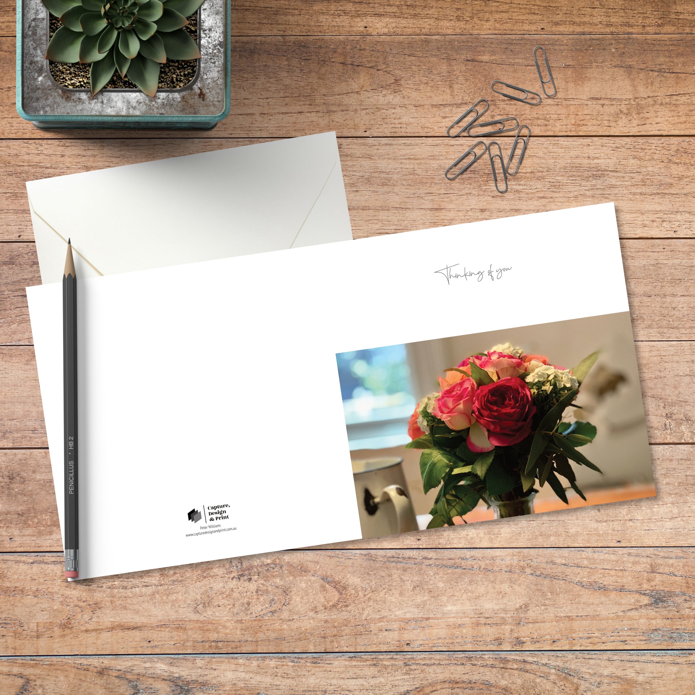 A small square greeting card in colour with full spread displayed on timber, featuring a vase of brightly coloured flowers