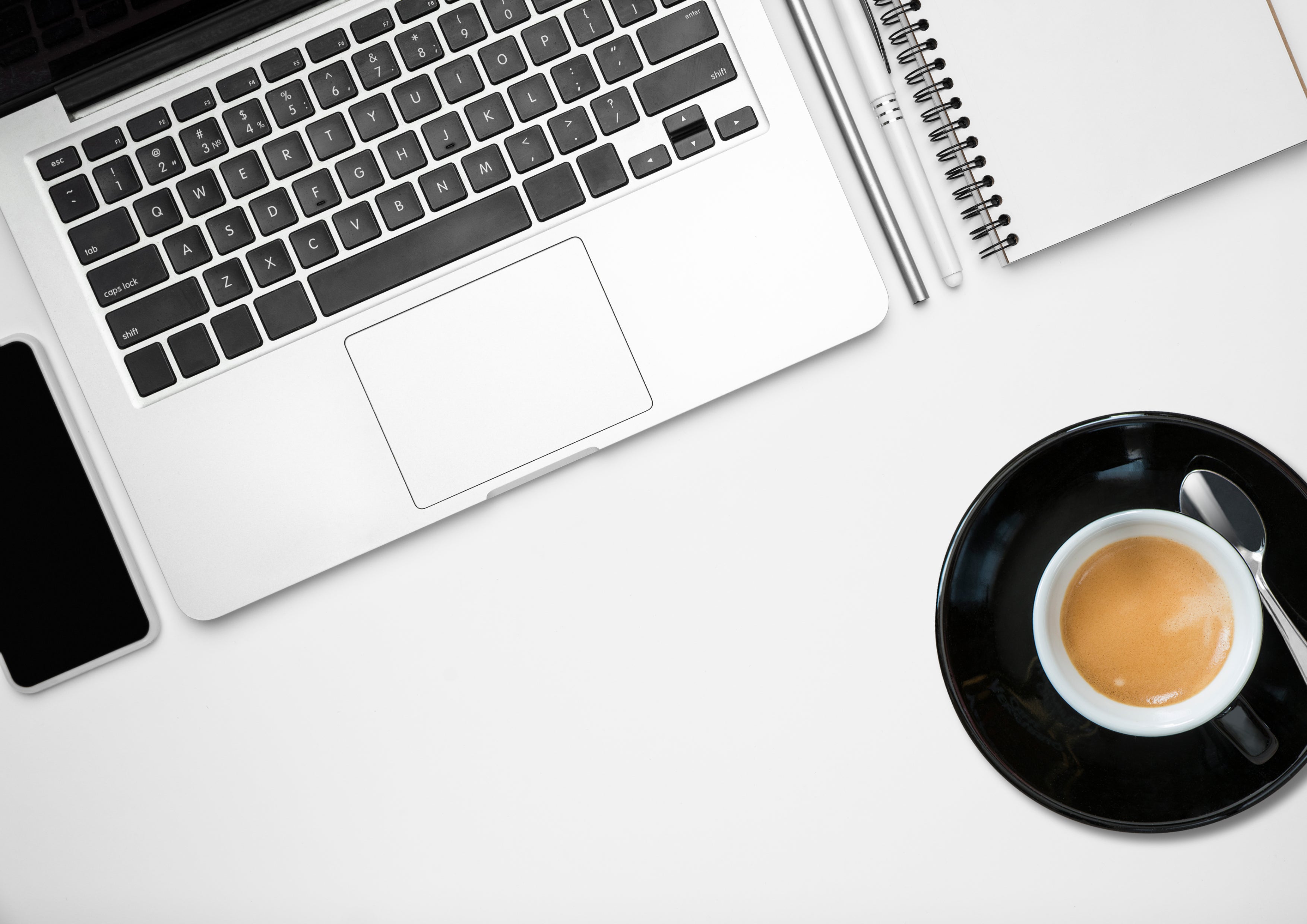 Workspace showing laptop, mobile phone, notebook, pens and cup of coffee